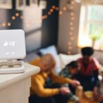 Smartes Thermostat zeigt 18 Grad Innentemperatur in einem gemütlichen Wohnzimmer, während eine Familie im Hintergrund spielt – Energieeffizienz und Heizkosten sparen durch intelligente Steuerung.