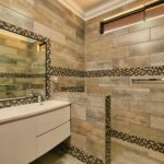 Modernes Badezimmer mit Holzoptik-Fliesen, schwarzen Mosaikbordüren, begehbarer Dusche und Waschtisch nach Sanierung