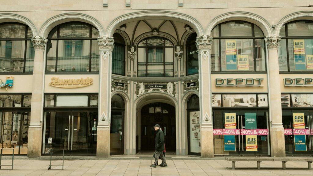 Klassische Gründerzeitfassade mit Bogenarkaden, Säulen und Kapitellen, historisches Ladengeschäft mit Schaufenstern und Rabattplakaten an der Straße