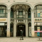 Klassische Gründerzeitfassade mit Bogenarkaden, Säulen und Kapitellen, historisches Ladengeschäft mit Schaufenstern und Rabattplakaten an der Straße