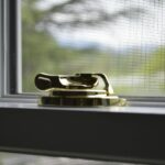 Fenstergriff mit Sicherheitsverriegelung auf Fensterrahmen mit Insektenschutzgitter zum Schutz vor Einbruch