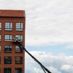 Arbeiter auf Hubsteiger führt Wartungsarbeiten an Fassade eines fünfgeschossigen Ziegelgebäudes durch