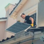 Handwerker montiert Solarpanel auf Hausdach mit Schutzhandschuhen während Sanierung und Solaranlage-Installation