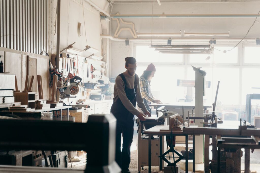 Handwerker in einer hellen Schreinerwerkstatt arbeiten an Holzprojekten an Werkbänken mit Maschinen und Werkzeugen