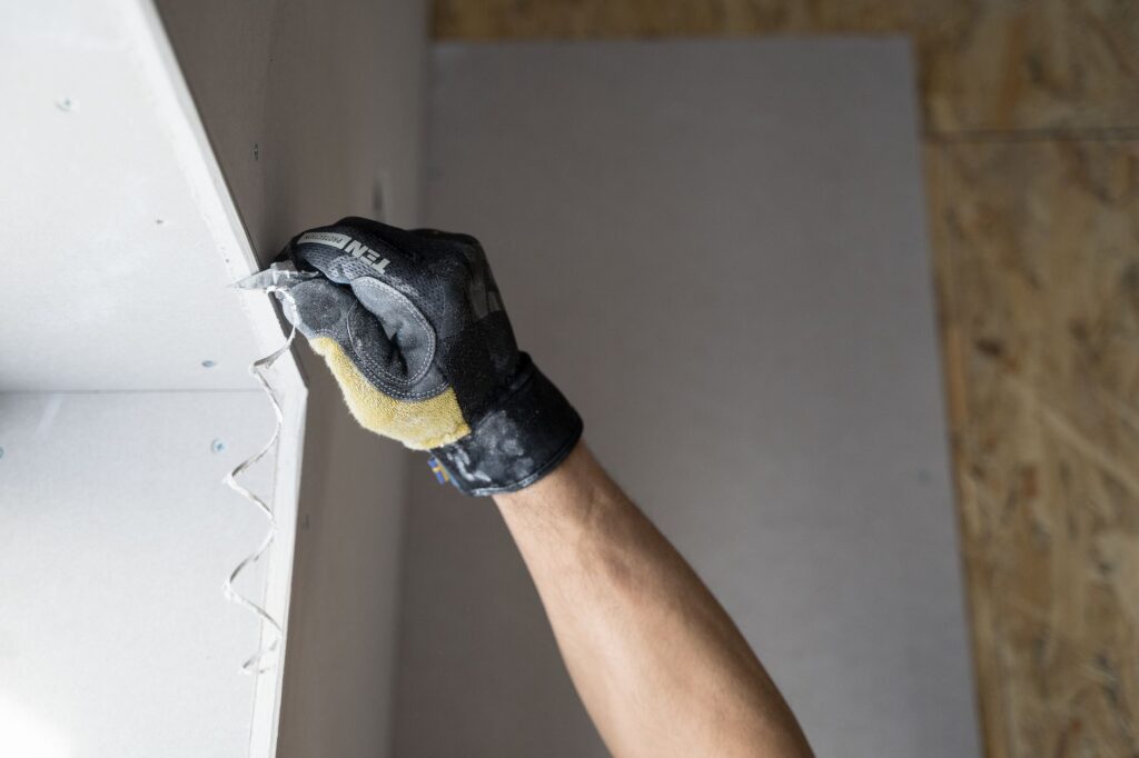 Handwerker in Schutzhandschuhen spachtelt Trockenbau-Fugen an Gipskartonplatten mit Spachtelmasse