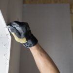 Handwerker in Schutzhandschuhen spachtelt Trockenbau-Fugen an Gipskartonplatten mit Spachtelmasse