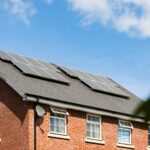 Rotes Backsteinhaus mit grauem Satteldach und Solarpanelen unter blauem Himmel – moderne Sanierung mit erneuerbaren Energien
