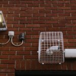 LED-Außenleuchte mit Bewegungsmelder an Ziegelmauer neben Abluftgitter und Steckdose für Einbruchschutz
