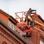 Dachdecker auf Hubarbeitsbühne bei Dacharbeiten an Ziegeldach mit Fallschutz gesichert
