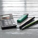 Taschenrechner, grüner Prüfstift und Kugelschreiber auf Holztisch zur Steuerberechnung für Photovoltaik