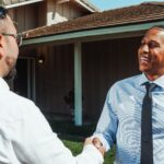Handwerker und Kunde schütteln sich vor modernisiertem Wohnhaus die Hand zur Besiegelung einer erfolgreichen Zusammenarbeit