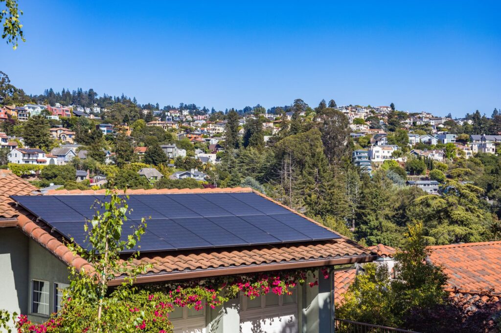 Solaranlage auf Terrakotta-Dachziegeln eines Wohnhauses in Hanglage mit Blick auf bewaldete Hügellandschaft und bunte Nachbarhäuser